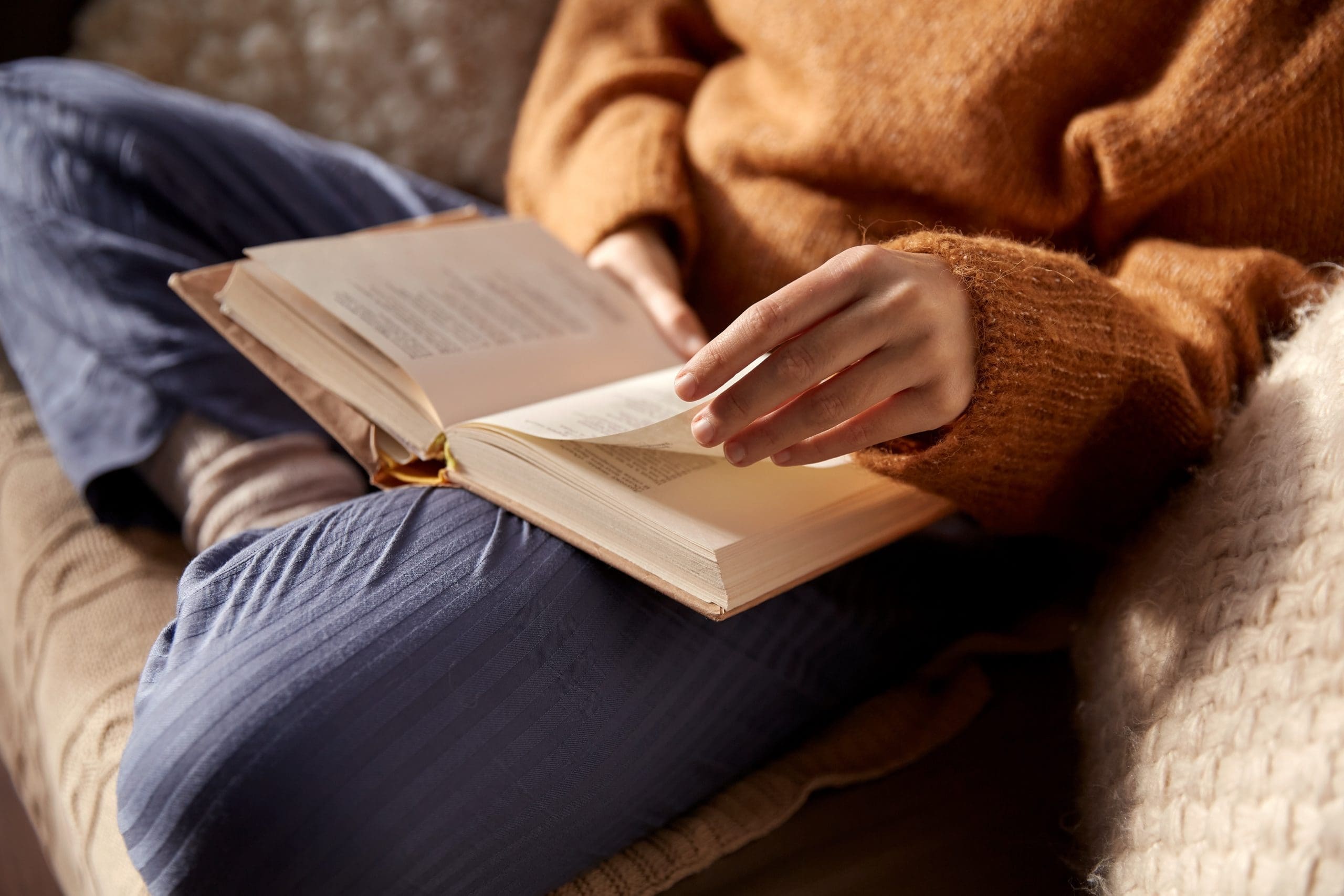 woman in warm sweater reading book at home
