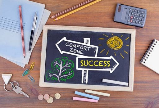 Comfort Zone - Success signpost drawn on a blackboard. sitting on a table with a calculator , notepad and pens next to it.