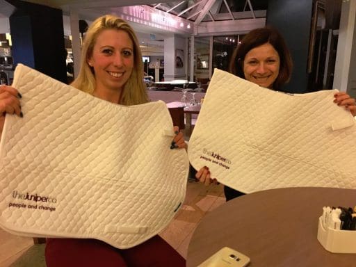 Ginny Howe and Nicki Kavanagh seated in a restaurant. Holding up The Juniper Co saddle pads
