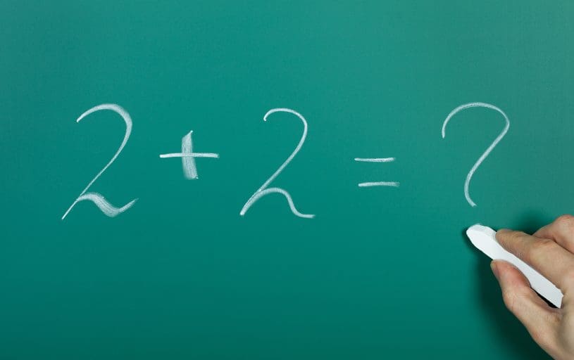 Hand writing 2 plus 2 Equals in chalk on a blackboard