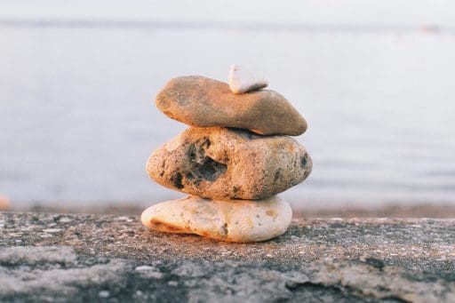 Three large pebbles on a beach , stacked in a tower with a small pebble on top . The Sea is in the background.