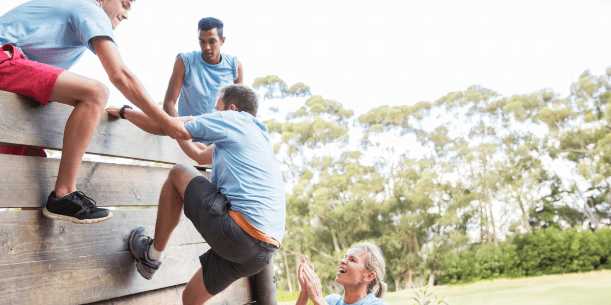 A group working together to help each other climb an outdoor obstacle wall